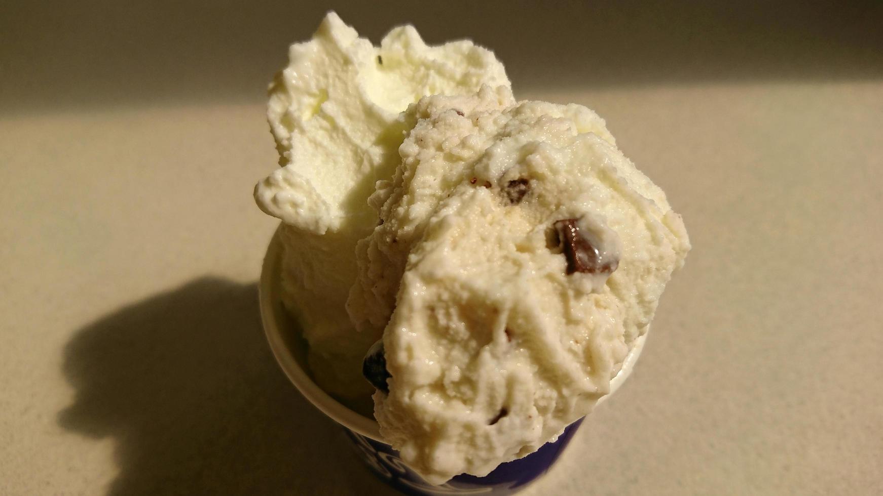 helado de vainilla y patrón de postre helado sabor chocolate en taza negra mano sujetando sobre madera y blanco. foto