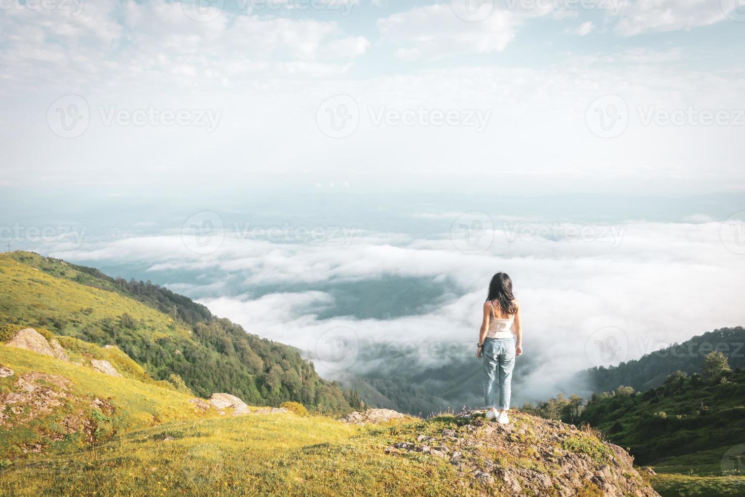 Solo brunette woman relaxed stands on the edge above clouds carefree lifestyle. Adventure and fullflment in life concept. photo