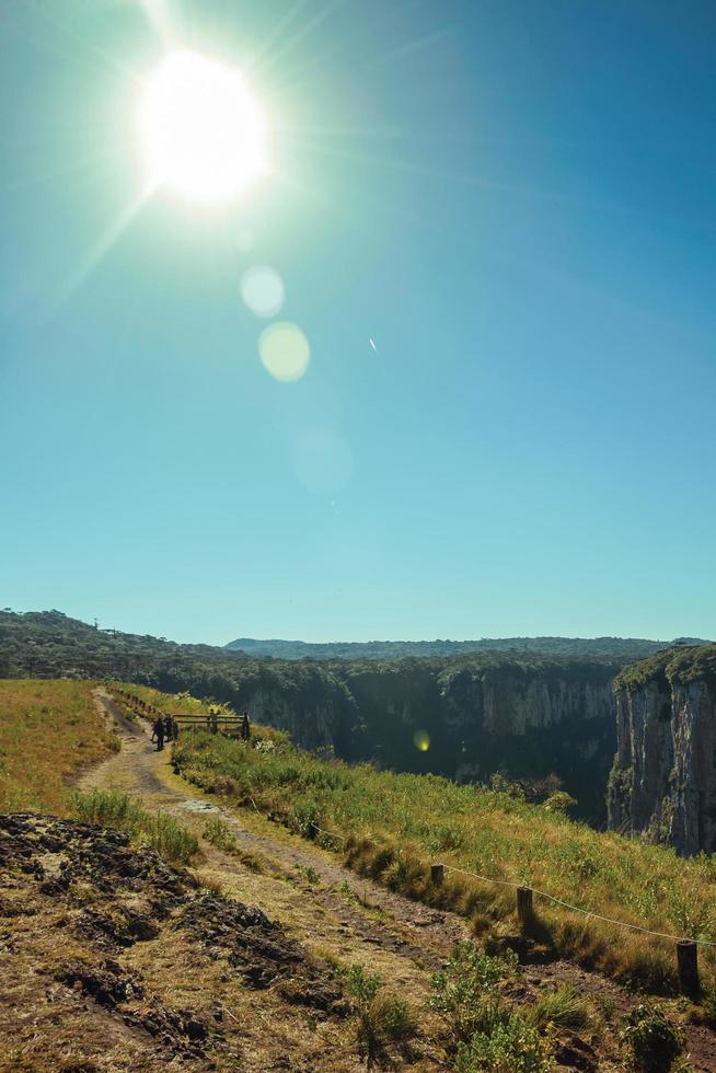 Dirt pathway and people at the Itaimbezinho Canyon with steep rocky cliffs and sunlight near Cambara do Sul. A small country town in southern Brazil with amazing natural tourist attractions. photo