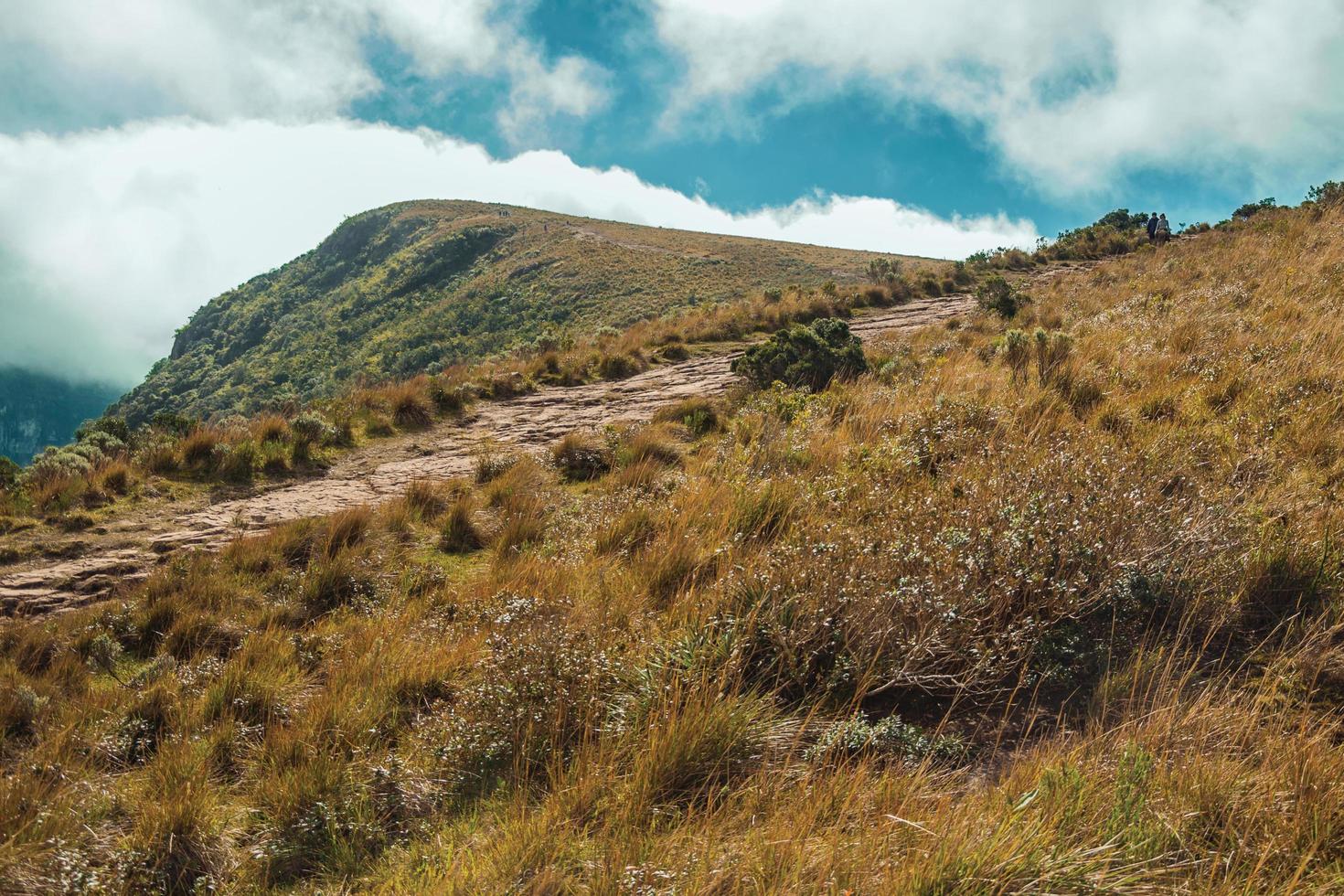 Rocky trail going up through dry bushes towards a cliff on top of Fortaleza Canyon in a sunny day near Cambara do Sul. A small country town in southern Brazil with amazing natural tourist attractions. photo