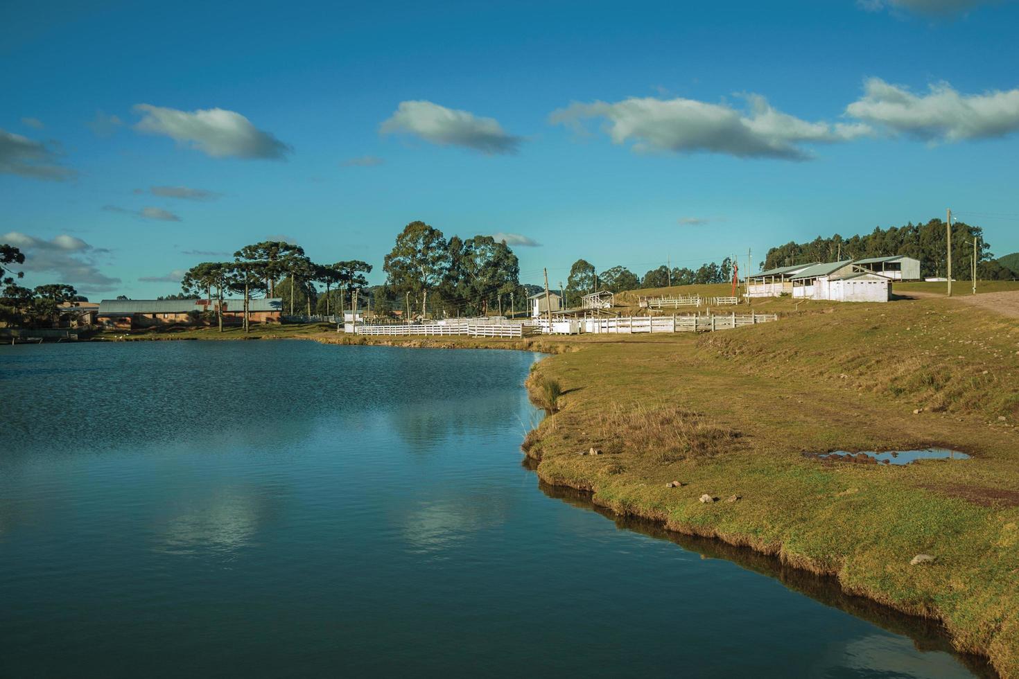 Pretty farm with fences, livestock sheds and blue lake on landscape of rural lowlands called Pampas at Cambara do Sul. A small country town in southern Brazil with amazing natural tourist attractions. photo