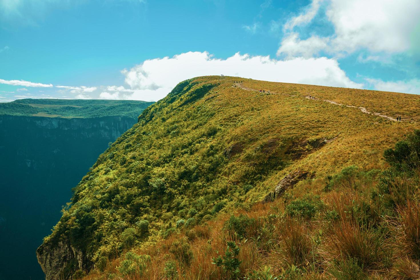 Rocky trail going up through dry bushes towards a cliff on top of Fortaleza Canyon in a sunny day near Cambara do Sul. A small country town in southern Brazil with amazing natural tourist attractions. photo