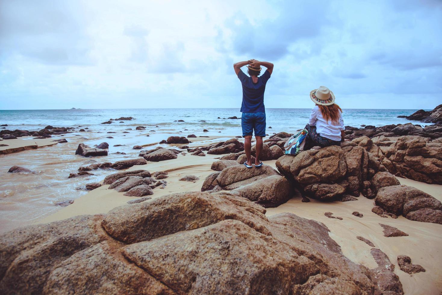 Asian lovers happy on the beach.The sky is bright Travel nature and sitting relax on the rocks at the sea at phuket. in Thailand. summer. photo