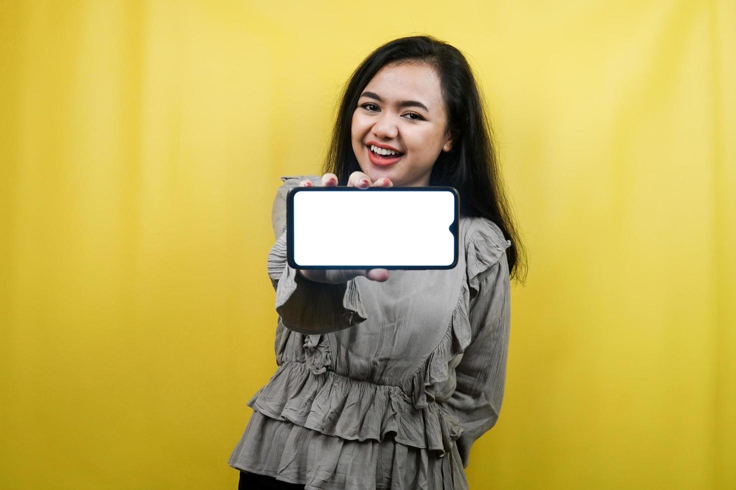 Hermosa mujer joven con las manos sosteniendo un teléfono inteligente con pantalla en blanco o en blanco, promoviendo el juego, promocionando la aplicación, alegre y confiada, publicidad, aislado foto