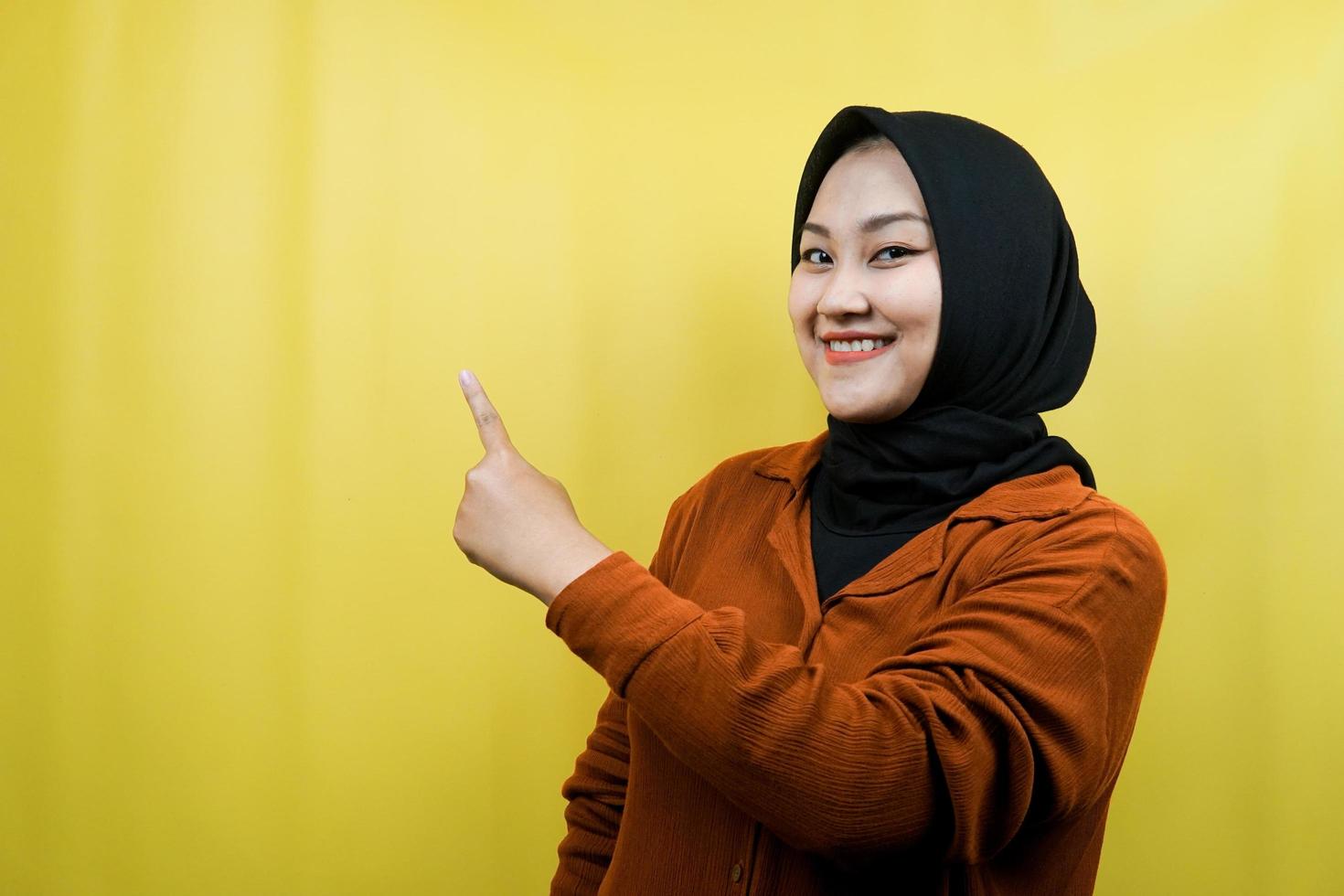 Beautiful young asian muslim woman with hands pointing empty space presenting something, smiling confident, enthusiastic, cheerful, looking at camera, isolated, advertising concept photo