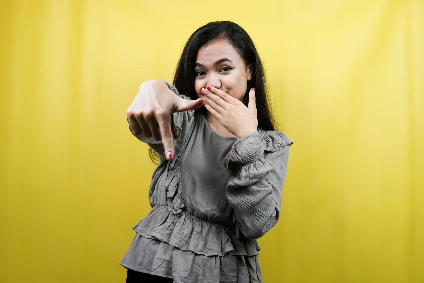 Beautiful young woman with hand covering mouth, hand pointing down, showing disapproval expression, showing disgust at something, isolated photo