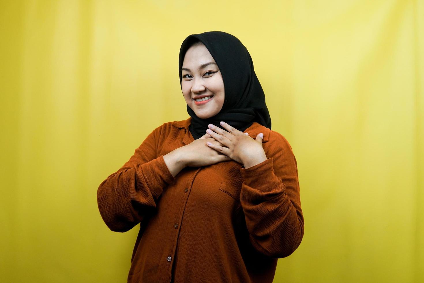 Beautiful and cheerful young asian muslim woman, with hands holding chest, isolated photo
