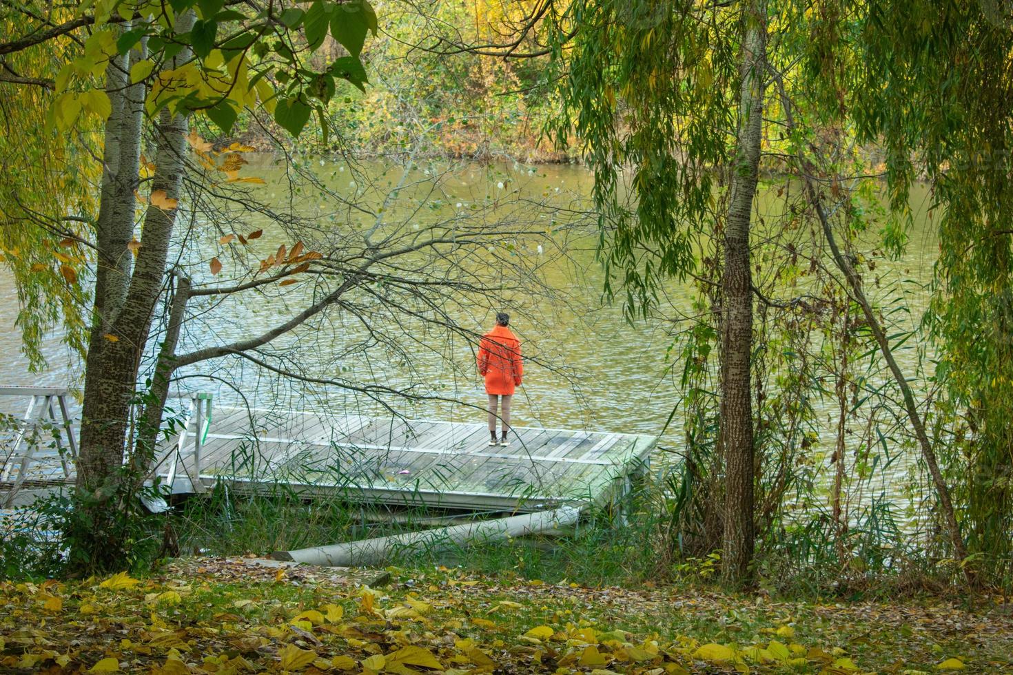 Mujer elegante en abrigo naranja mirando en la orilla del río foto