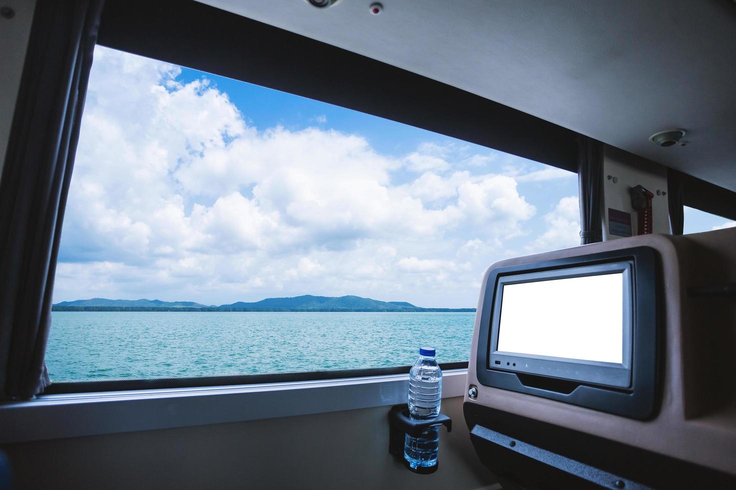 Inside of the bus which has LCD screen blank rear seat for entertainment with a bottle of water and window view of Beautiful landscape nature the sea with sky cloud, Figure tourism road trip concept. photo