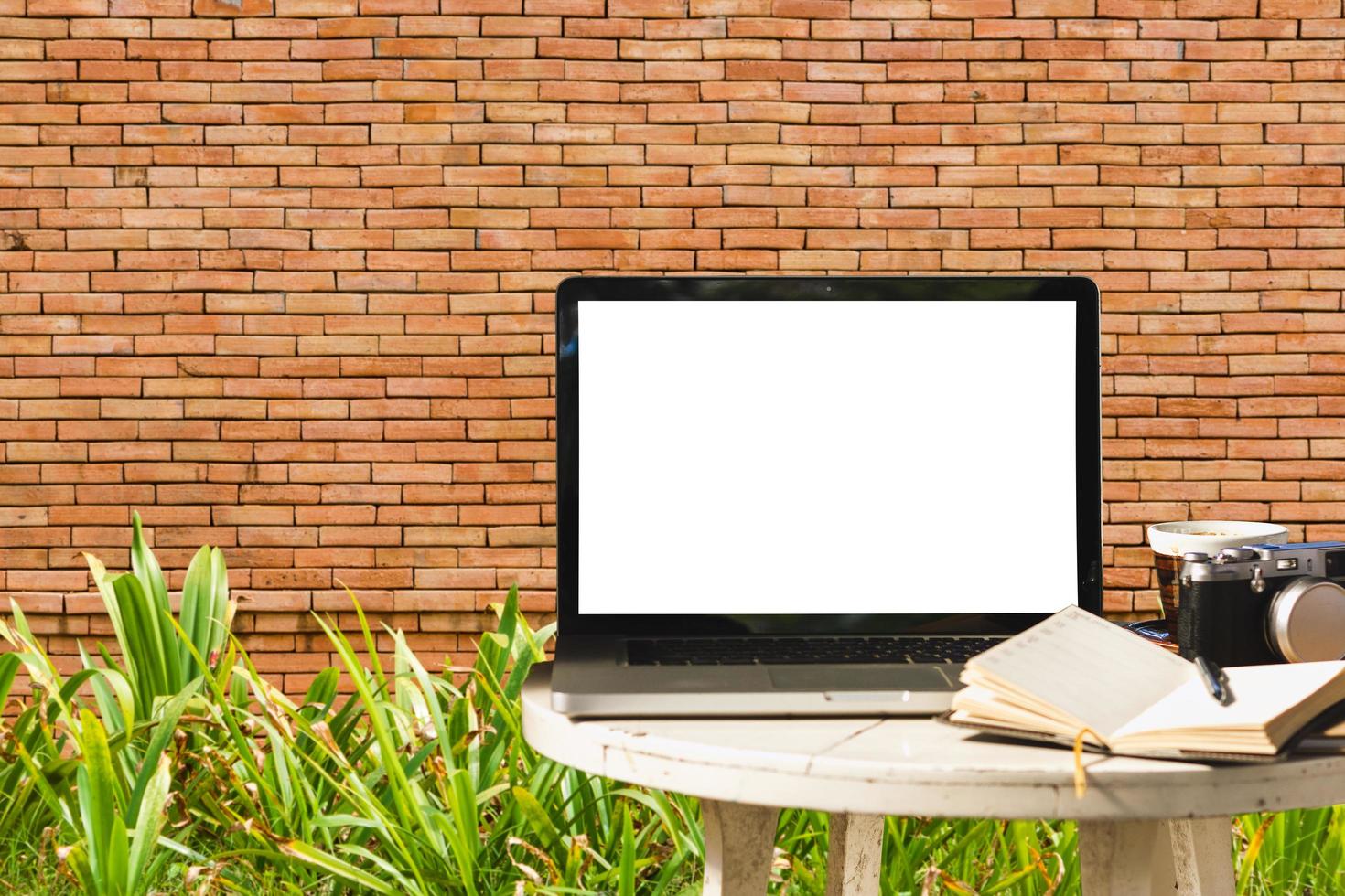 Mockup image of laptop with blank black screen with camera,notebook,coffee cup on wooden table with wall large texture background. photo