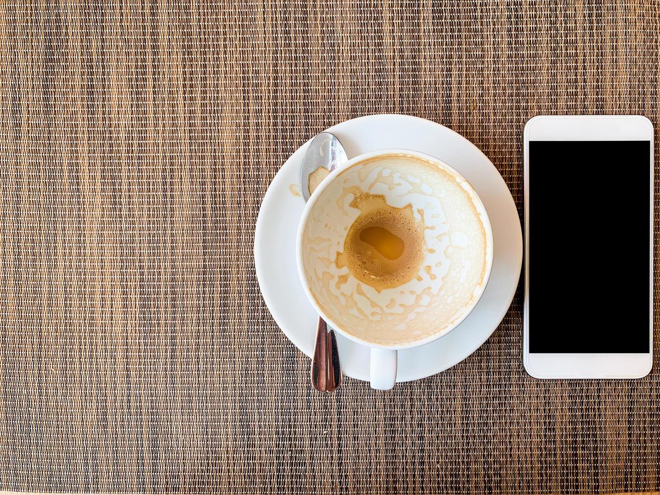 teléfono inteligente y taza de café vacía en el escritorio de madera en la vista superior. foto