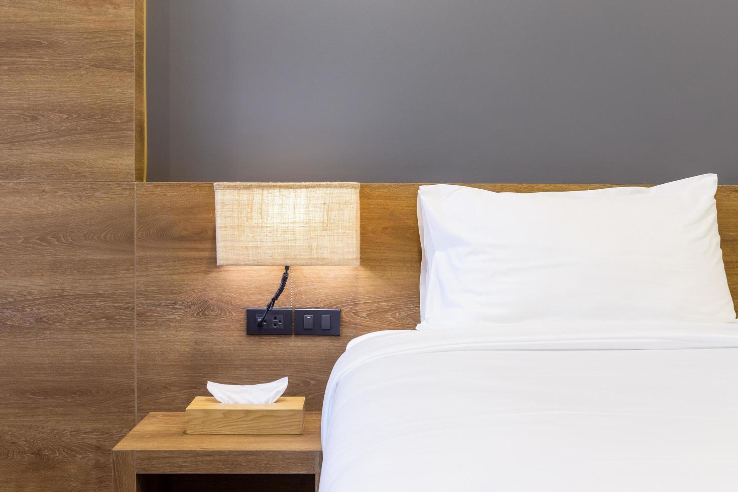 Close-up of white pillow on bed decoration with light lamp and tissue box in hotel bedroom interior. photo