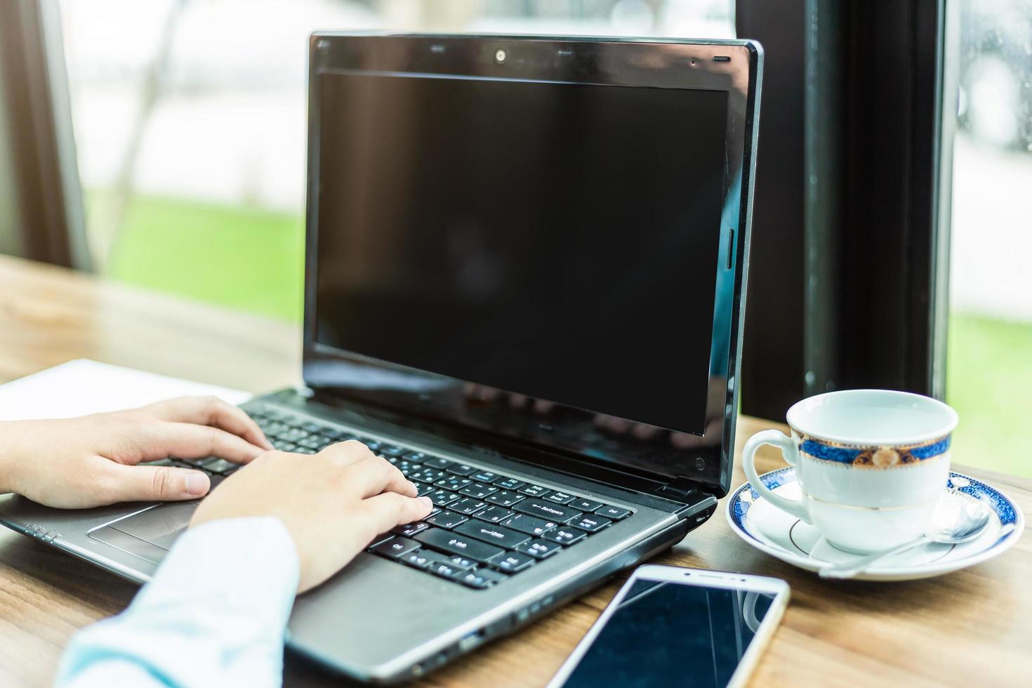 Close-up of Business woman working with smartphone,laptop with blank white screen and document in coffee shop like the background. photo
