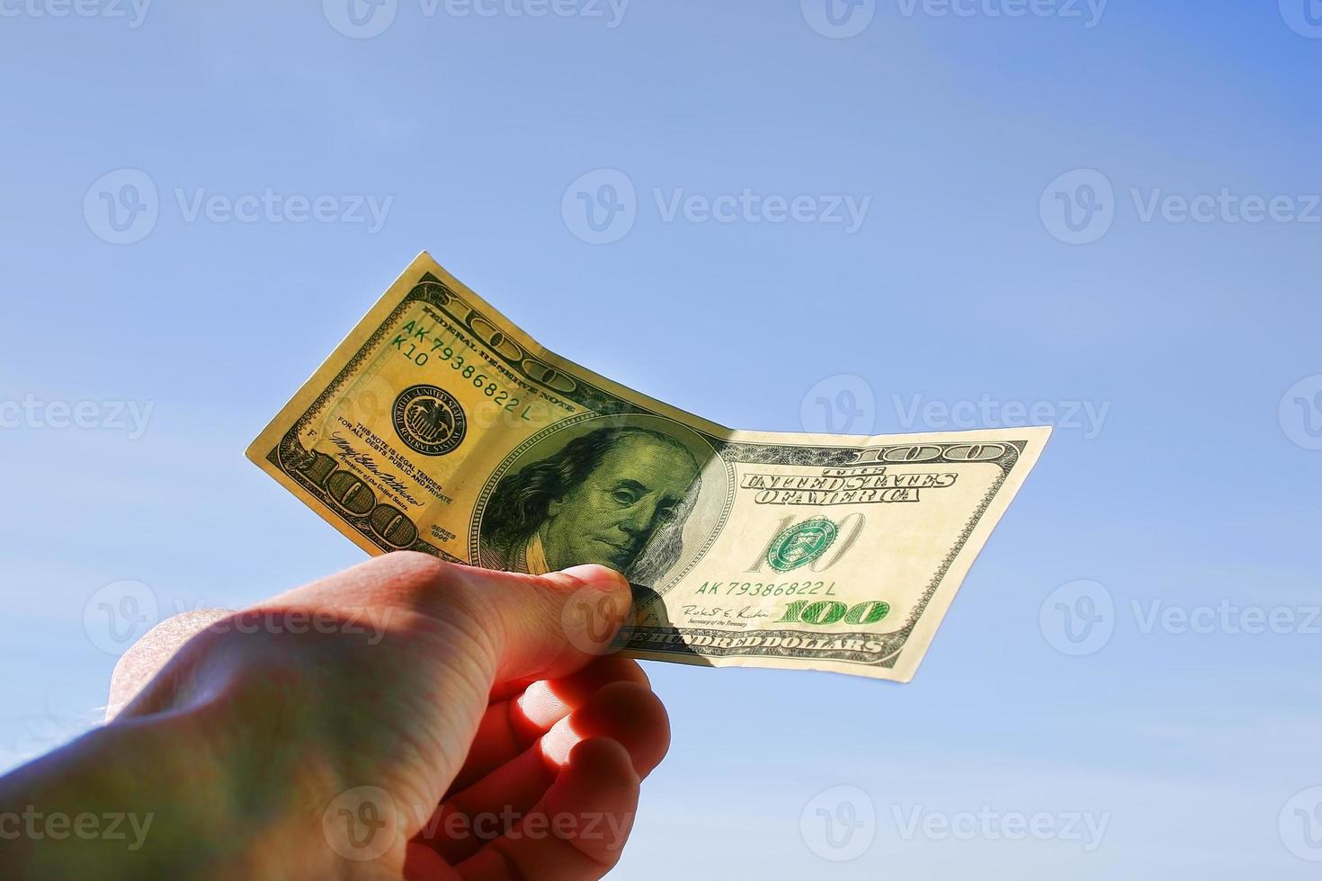 Holding a United States one-hundred-dollar bill against blue sky background photo