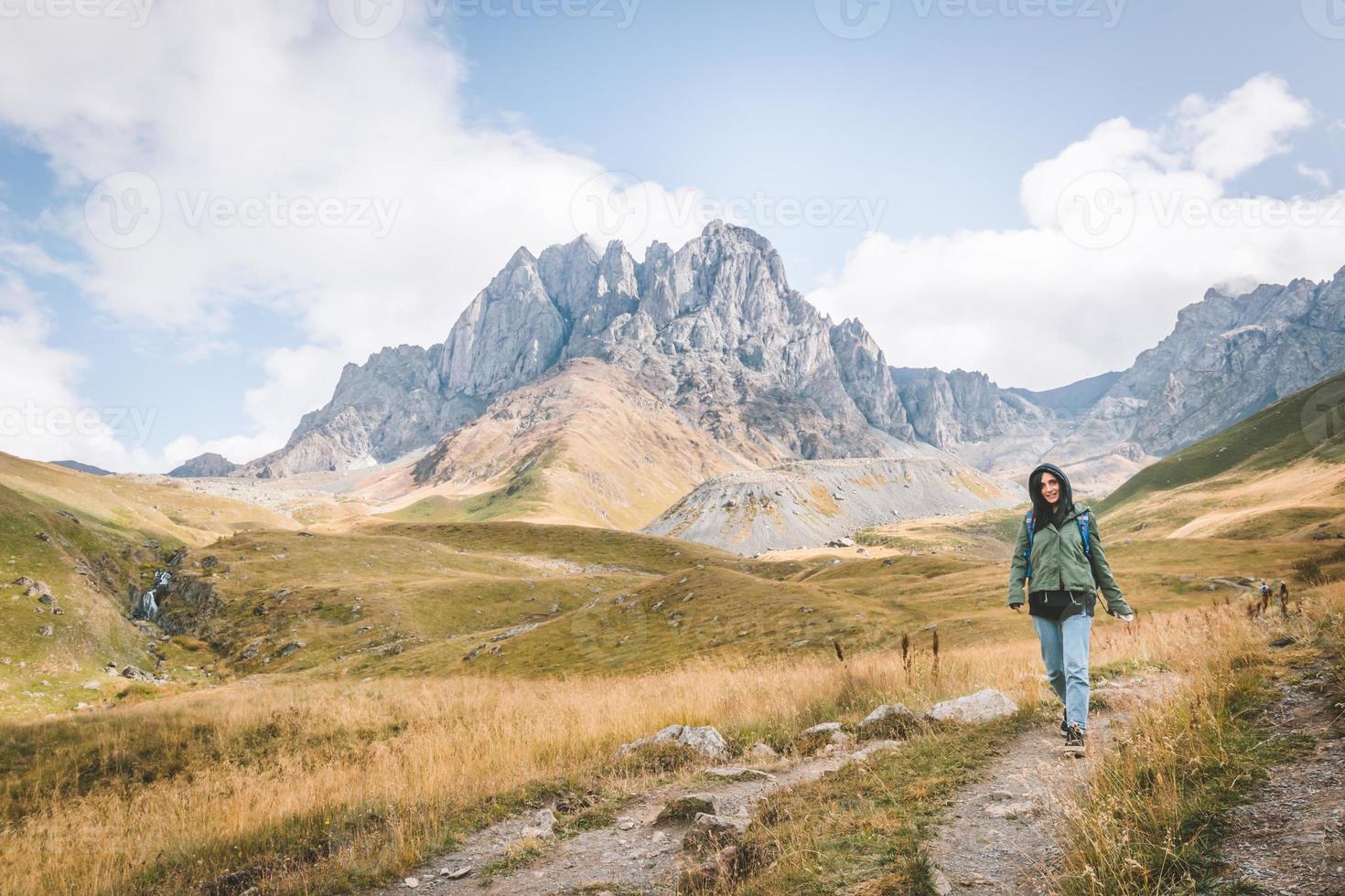 feliz mujer caucásica camina por el camino en el valle de juta con pintorescos paisajes montañosos. destino de viaje de kazbegi foto