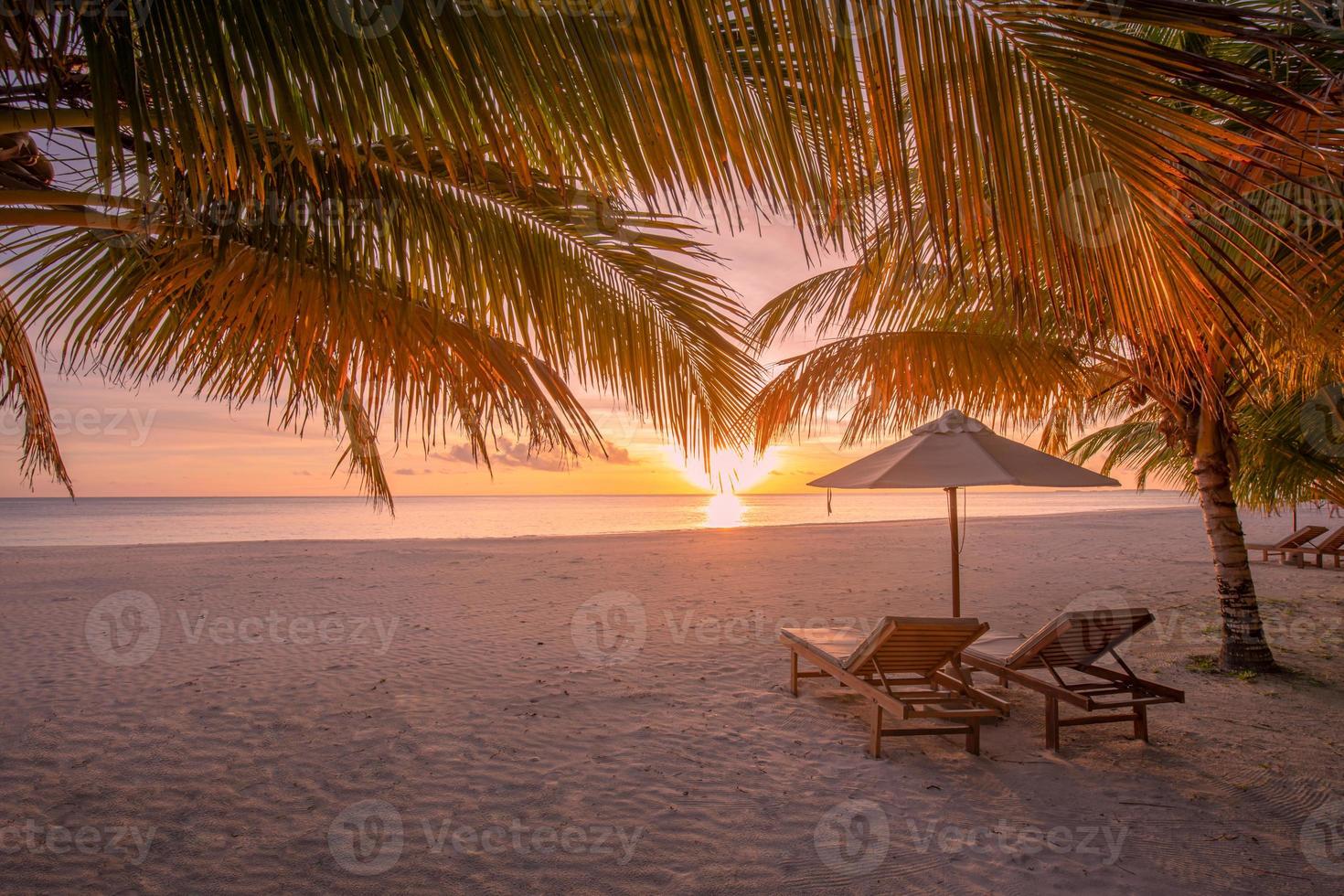 Beautiful tropical sunset scenery, two sun beds, loungers, umbrella under palm tree. White sand, sea view with horizon, colorful twilight sky, calmness and relaxation. Inspirational beach resort hotel photo