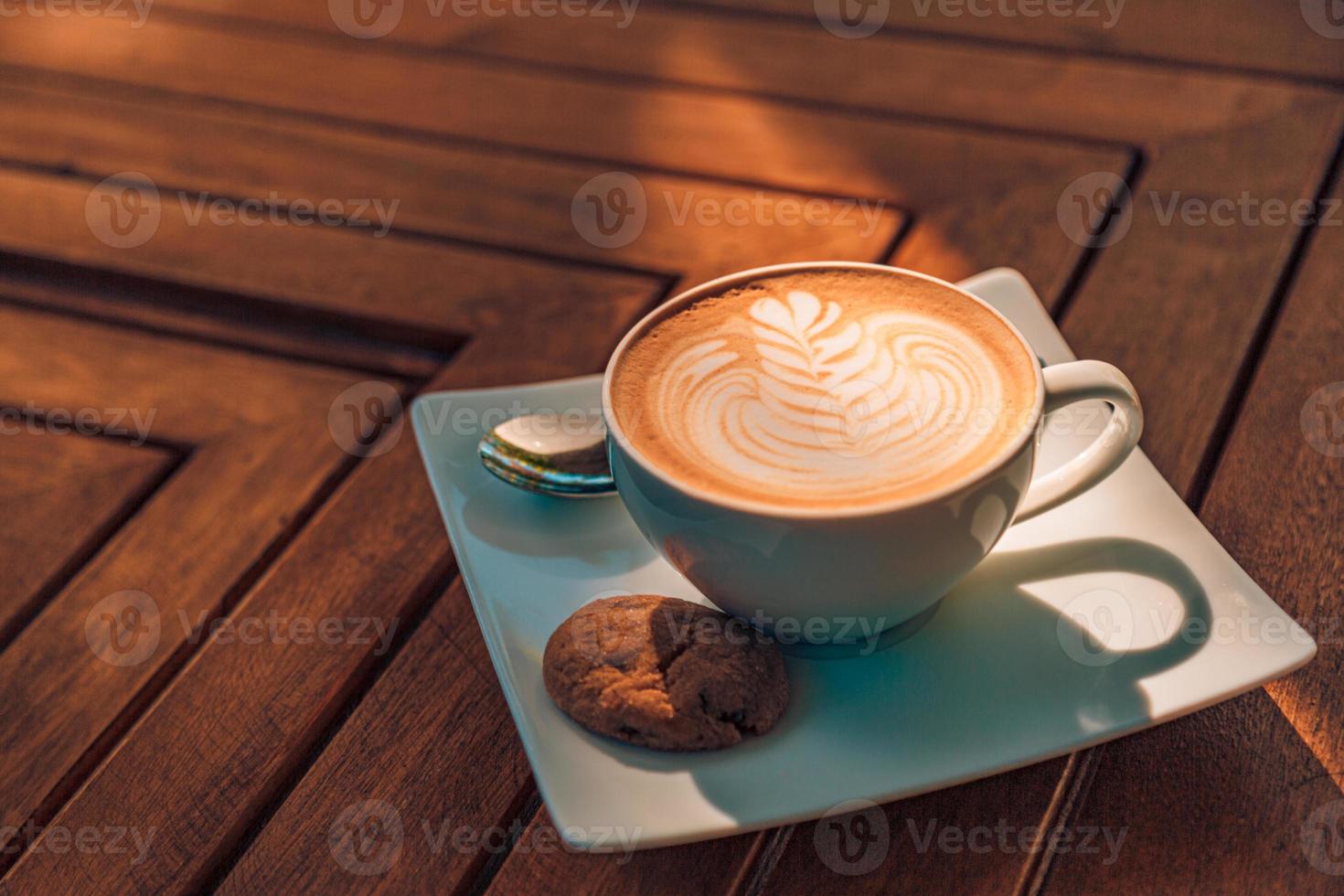 Cerrar una taza de café con leche capuchino caliente con arte latte en forma de corazón en una mesa de madera vieja de color marrón oscuro en el concepto de cafetería, comida y bebida. foto