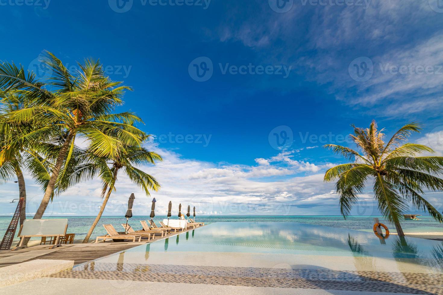 Outdoor tourism landscape. Luxurious beach resort with swimming pool and beach chairs or loungers under umbrellas with palm trees and blue sky. Summer travel and vacation background concept photo