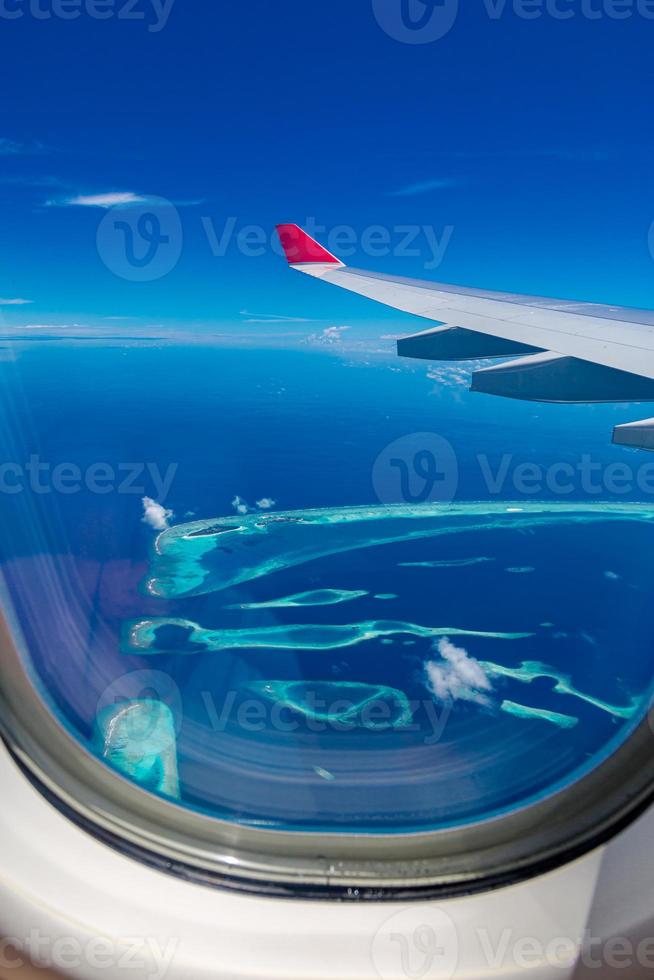 ventana de avión con hermosas vistas a la isla de Maldivas. Fondo de turismo de viajes de vacaciones de verano de lujo, vista desde la ventana del avión. atolones e islas con increíble mar tropical foto