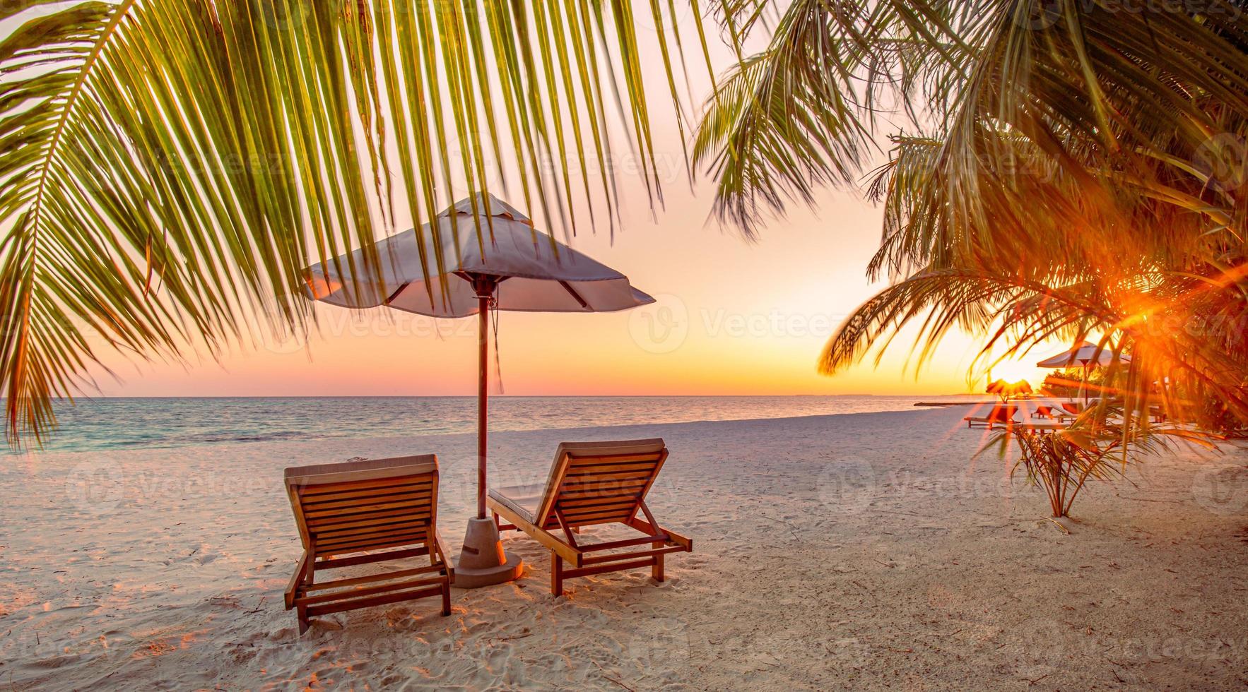 Beautiful tropical sunset scenery, two sun beds, loungers, umbrella under palm tree. White sand, sea view with horizon, colorful twilight sky, calmness and relaxation. Inspirational beach resort hotel photo