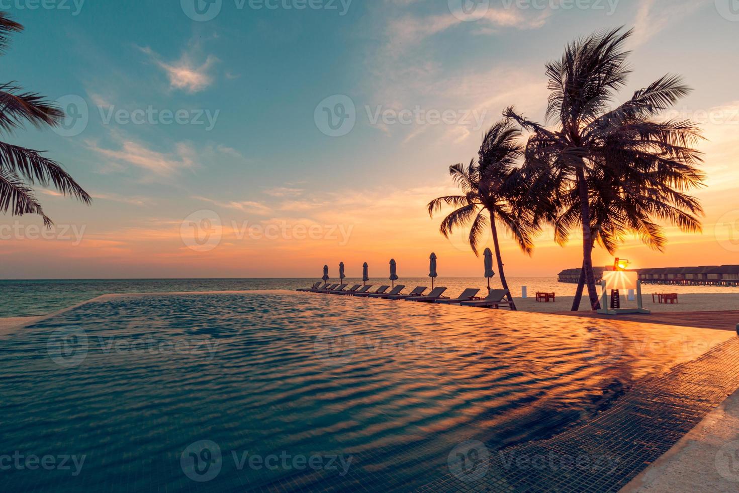 Luxury pool sunset, palm tree silhouette with windy infinity pool water surface. Summer vacation, holiday template. Stunning sky, beachfront hotel resort at tropical landscape tranquil. Amazing island photo