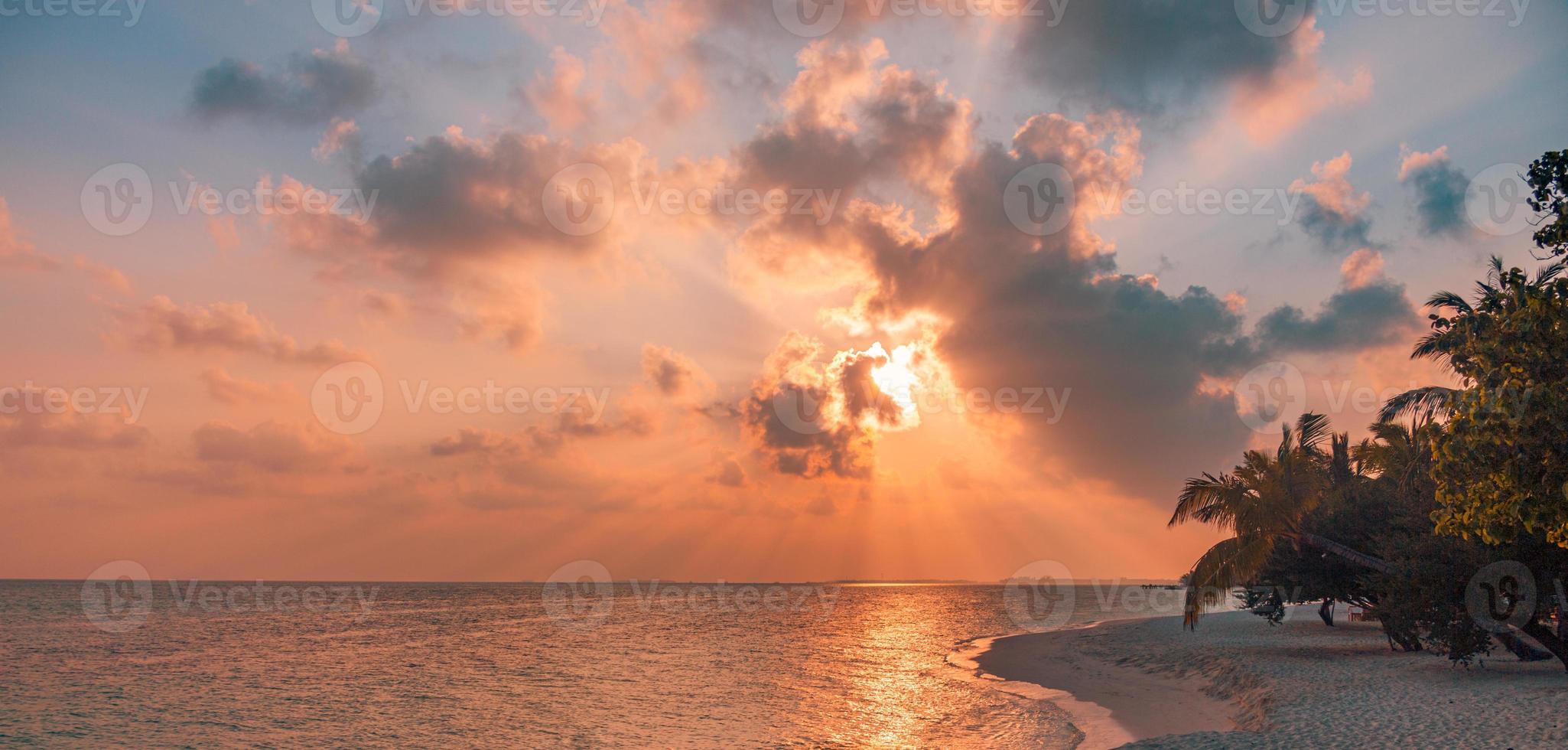 Fantastic sunset beach scene. Colorful sky and clouds view with calm sea and relaxing tropical mood. Sun rays, romantic paradise island landscape, palm silhouette, amazing beach evening photo