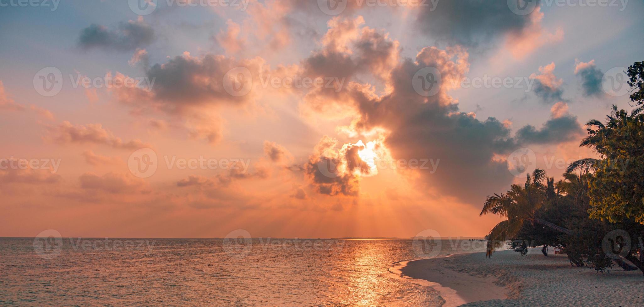 fantástica escena de playa al atardecer. Vista colorida del cielo y las nubes con un mar en calma y un ambiente tropical relajante. rayos de sol, romántico paisaje de la isla paradisíaca, silueta de palmera, increíble noche de playa foto