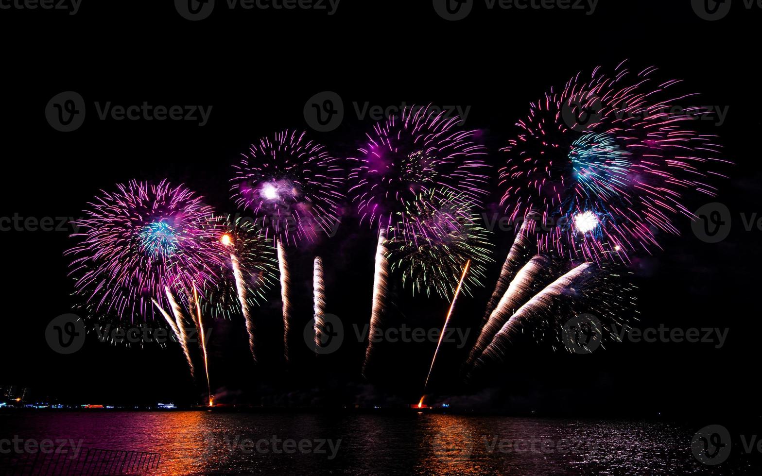 Increíble y hermoso colorido espectáculo de fuegos artificiales en la noche de celebración, que se muestra en la playa del mar con reflejos multicolores sobre el agua foto