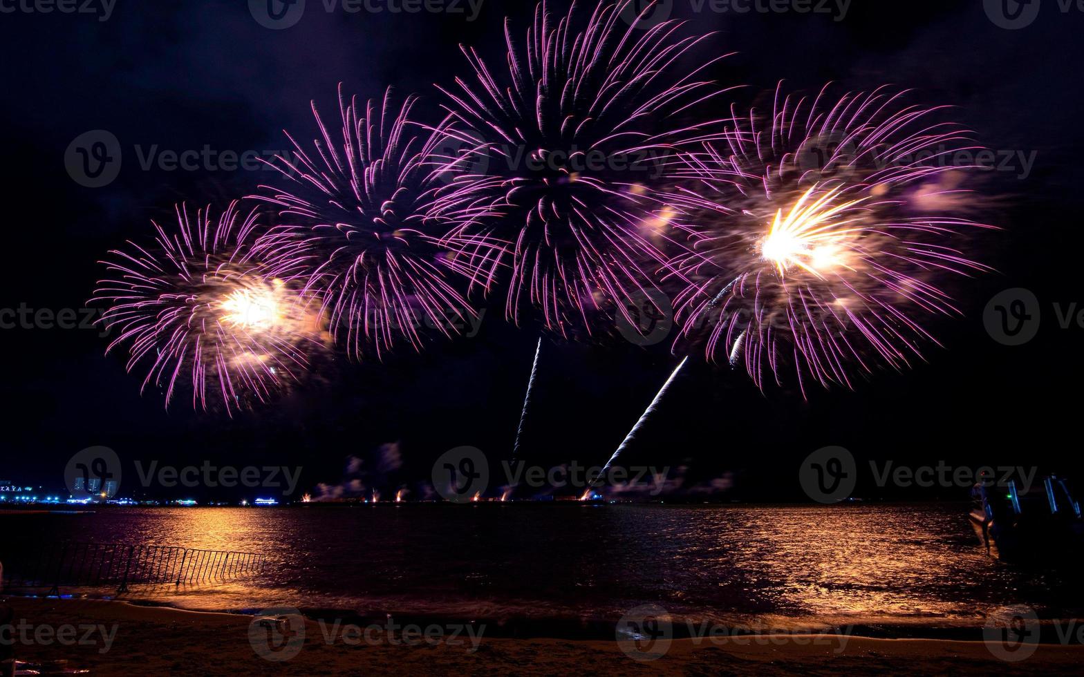 Increíble y hermoso colorido espectáculo de fuegos artificiales en la noche de celebración, que se muestra en la playa del mar con reflejos multicolores sobre el agua foto