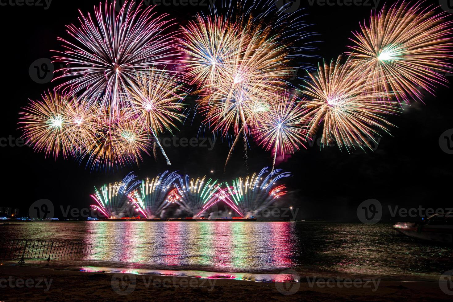 Increíble y hermoso colorido espectáculo de fuegos artificiales en la noche de celebración, que se muestra en la playa del mar con reflejos multicolores sobre el agua foto