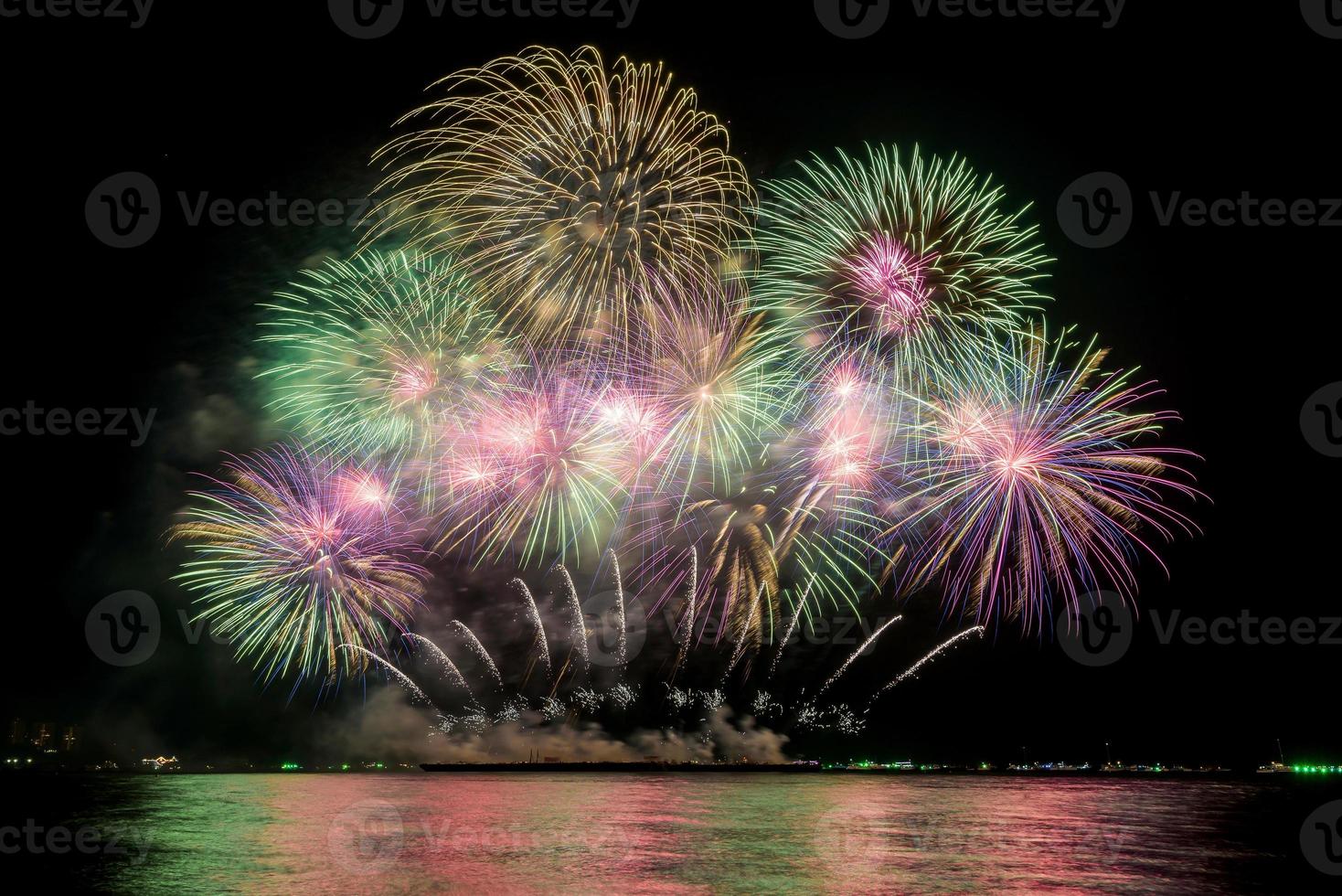 Increíble y hermoso colorido espectáculo de fuegos artificiales en la noche de celebración, que se muestra en la playa del mar con reflejos multicolores sobre el agua foto