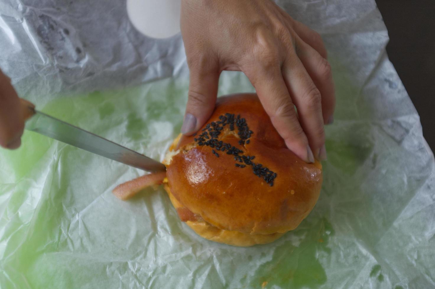 mano sosteniendo un pan de hamburguesa y cortando por la mitad foto