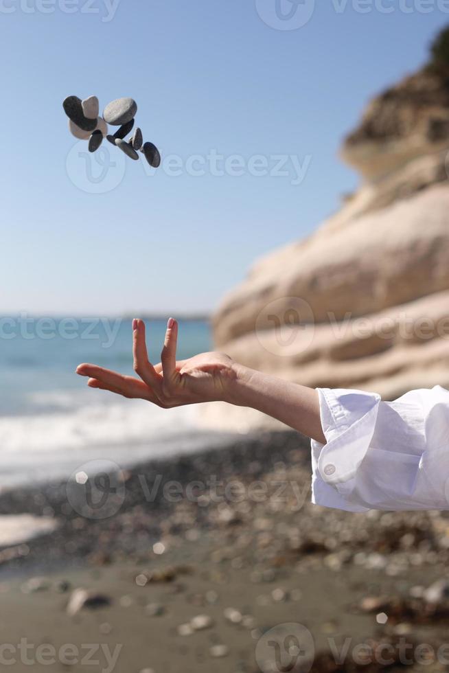 mano femenina lanza un guijarro en su mano contra el fondo del cielo azul, la playa, la roca y el mar. foto