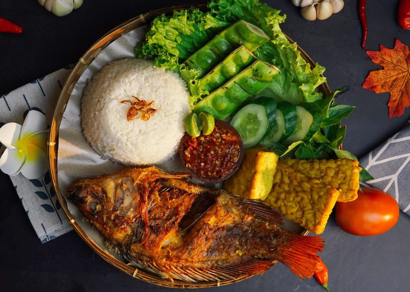 un paquete de arroz, pescado frito y algunas verduras frescas sobre un fondo negro foto