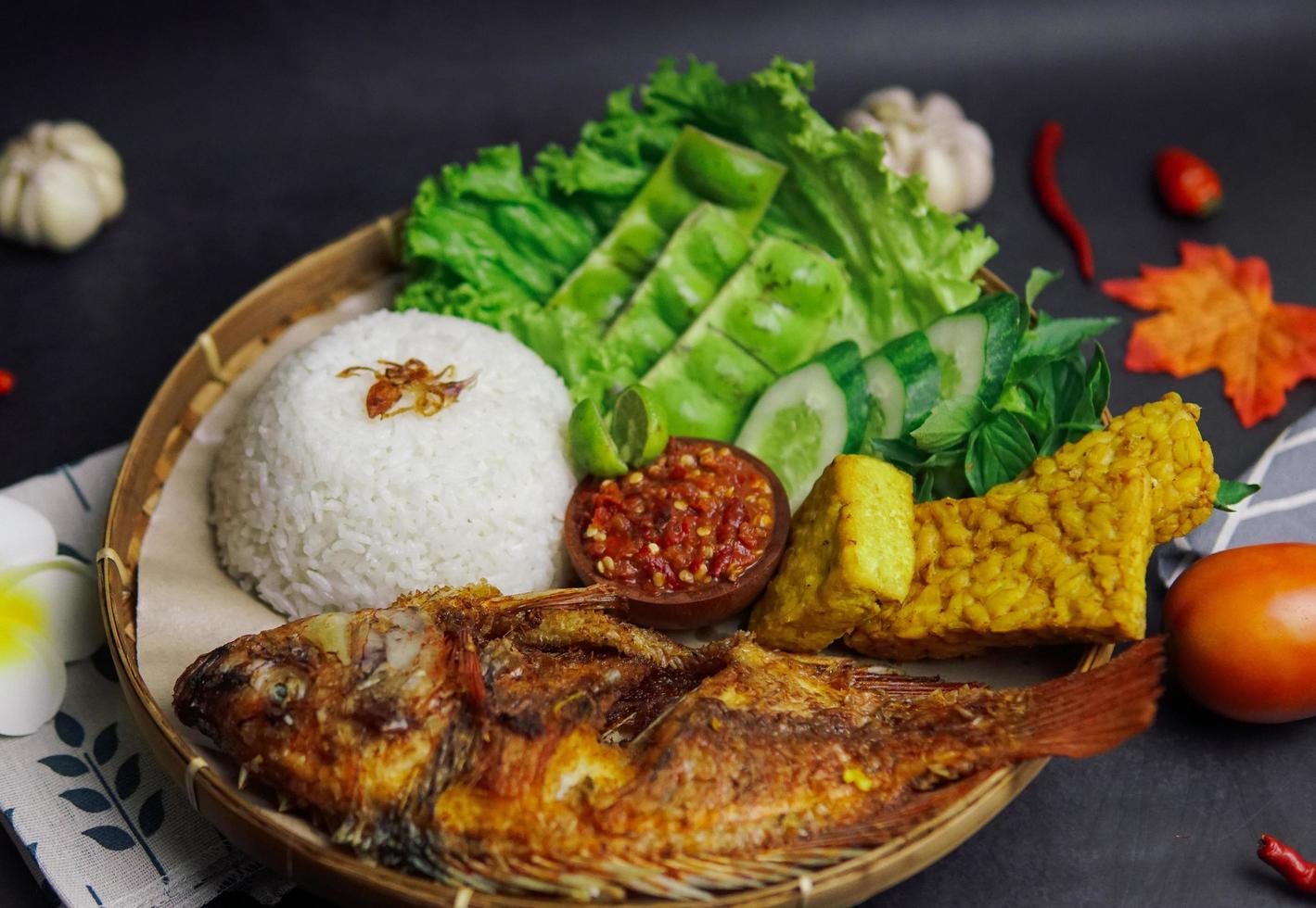 un paquete de arroz, pescado frito y algunas verduras frescas sobre un fondo negro foto