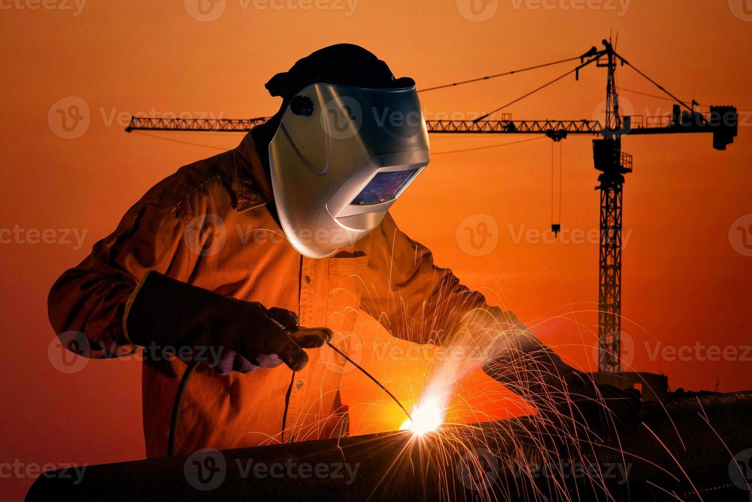 Welding worker welding steel structure with construction crane and building at construction site on sunset for construction industrial work concept. photo