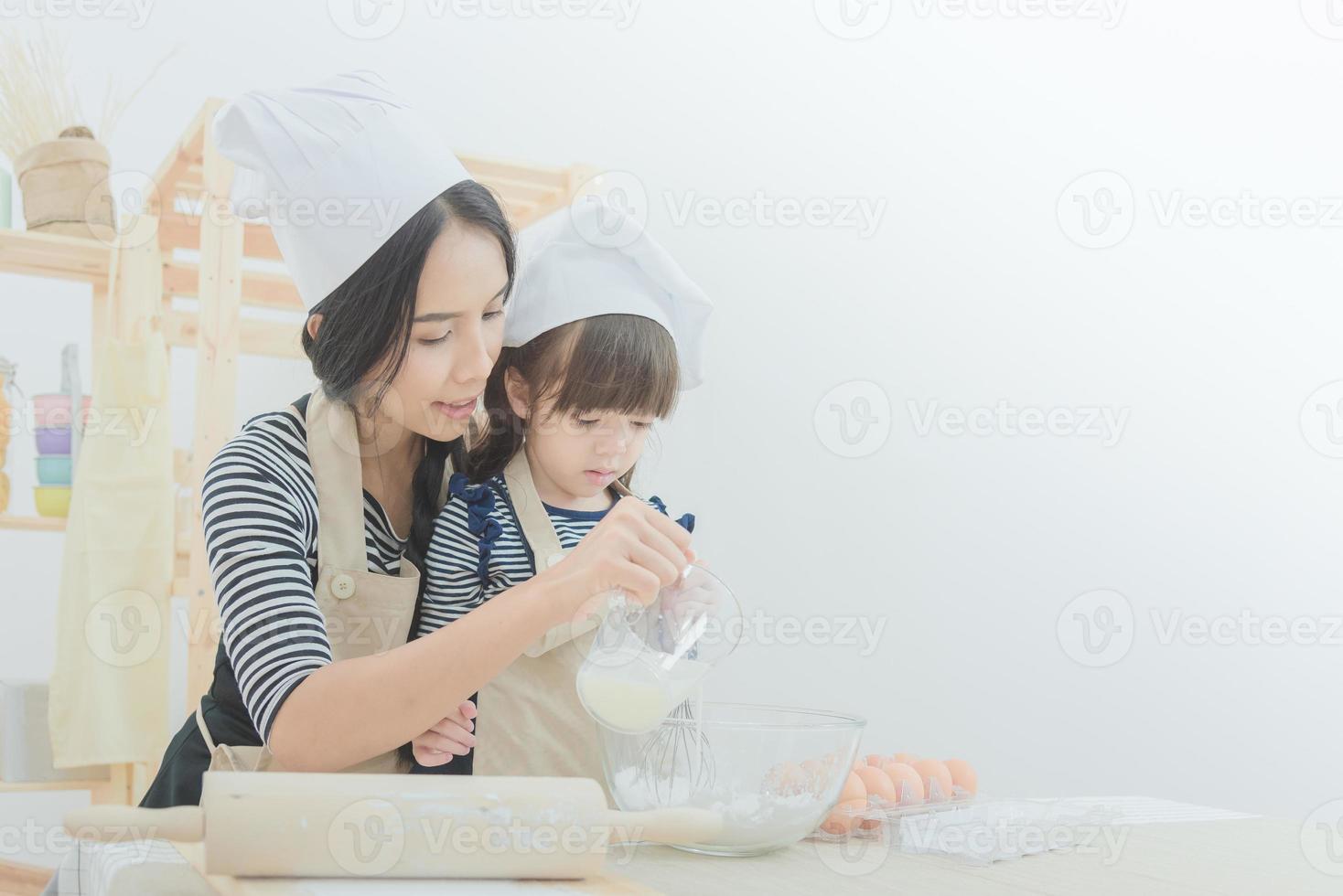 Happy family in the kitchen. Asian mother and her daughter preparing the dough to make a cake.Photo design for family, kids and happy people concept. photo