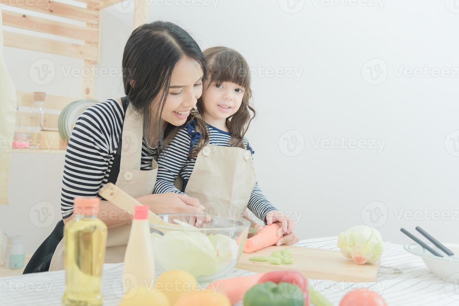 La madre asiática de la familia amorosa feliz y su hija preparan la ensalada de la comida sana en la sala de la cocina.Diseño de la foto para la familia, los niños y el concepto de la gente feliz.