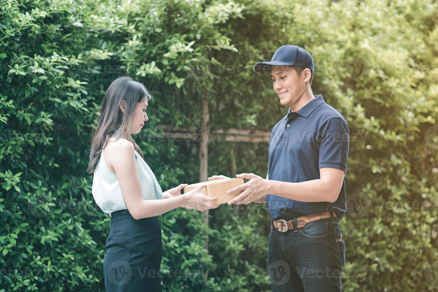 Handsome young asian delivery man smiling and giving a cardboard box to his customer photo