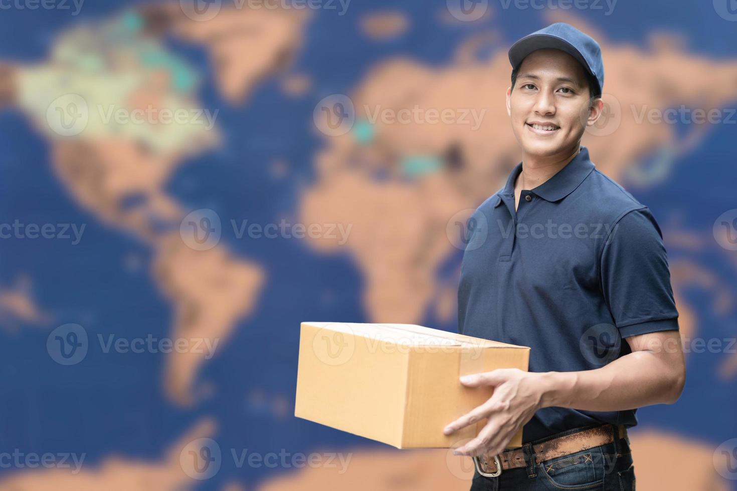 Repartidor asiático sosteniendo una caja de cartón con un mapa global en segundo plano para el comercio electrónico y el concepto de logística. foto