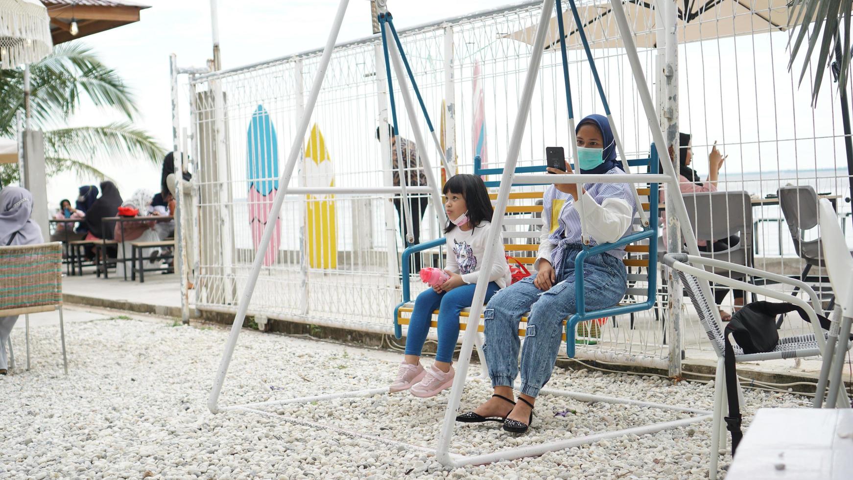 Pekanbaru, Indonesia 2020 - A woman is playing on a swing in the park and holding a smartphone photo