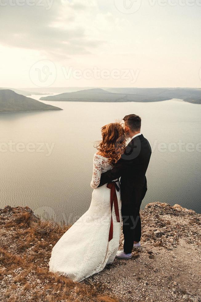Amazing wedding couple, bride and groom holding hands on a mountains and river background photo