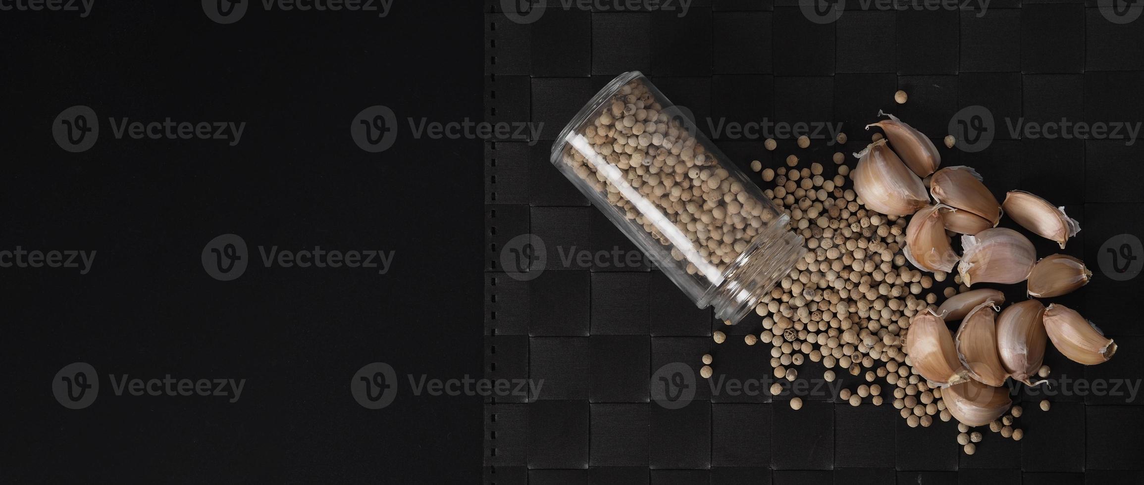 Natural Garlics and white peppercorn in glass bottle on plate mat black background. photo