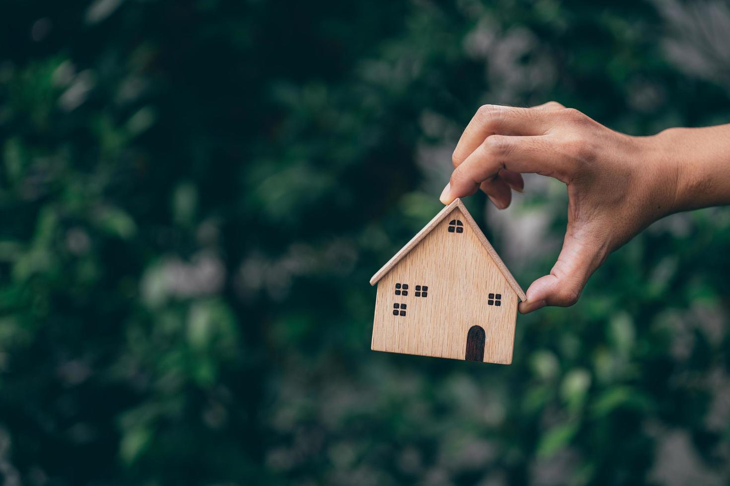 mano sosteniendo el modelo de la casa en el fondo de la naturaleza, ahorrando dinero en casa o préstamo para planificar la inversión empresarial por concepto de bienes raíces. foto