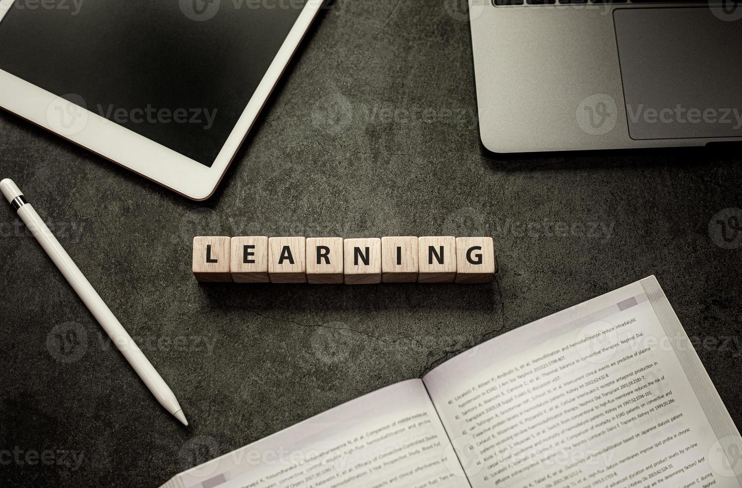 Blank screen tablet, pen, laptop, textbook and word learning on wood cube block on black table background photo