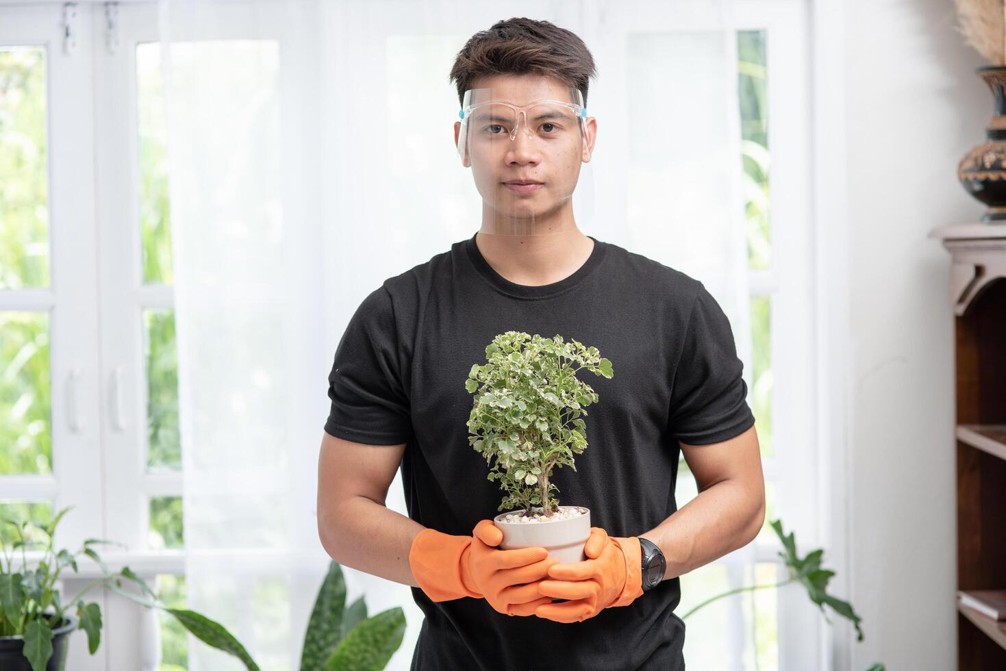 A man wears orange gloves and stands to hold a plant pot in the house. photo