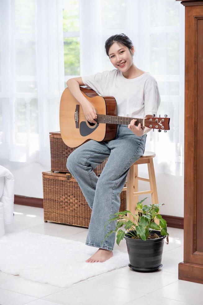 The girl is sitting and playing the guitar on the chair. photo