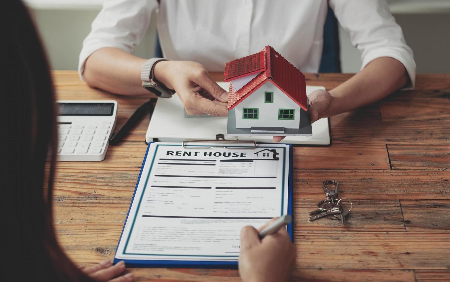 agente de bienes raíces y clientes están firmando acuerdos de compra de vivienda. mano que sostiene el contrato de compra de firma de pluma. Casas de techo gris y llaves colocadas cerca una de la otra. foto