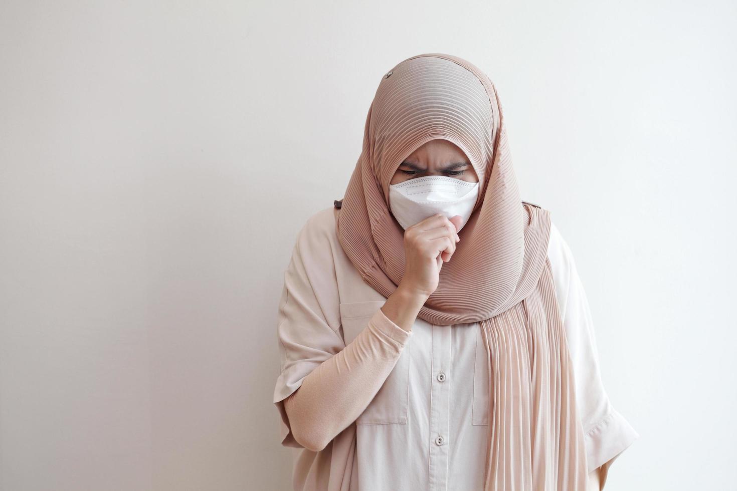 Mujer musulmana que llevaba una mascarilla quirúrgica sintiéndose enferma sobre fondo pastel. concepto de coronavirus covid-19. foto