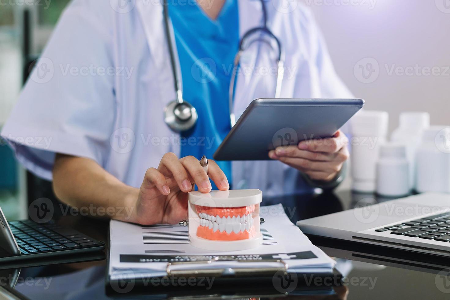 Concentrated dentist sitting at table with jaw samples tooth model and working with tablet and laptop in dental office professional dental clinic. photo